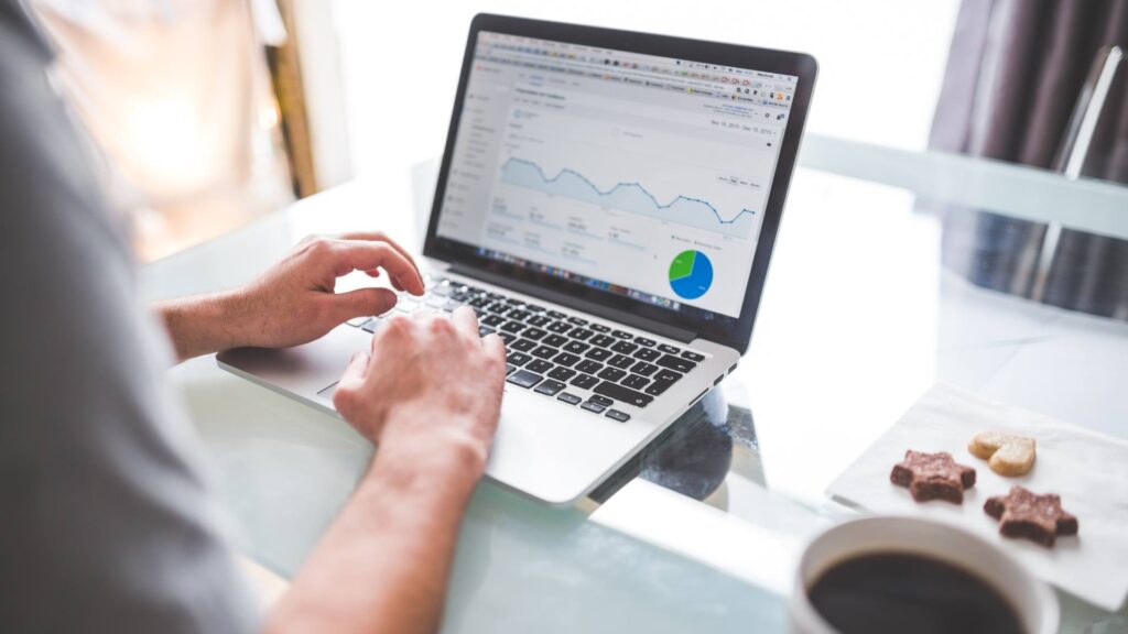 A person works on a laptop computer while doing a website SEO analysis. A cup of coffee and some cookies are displayed on the side.