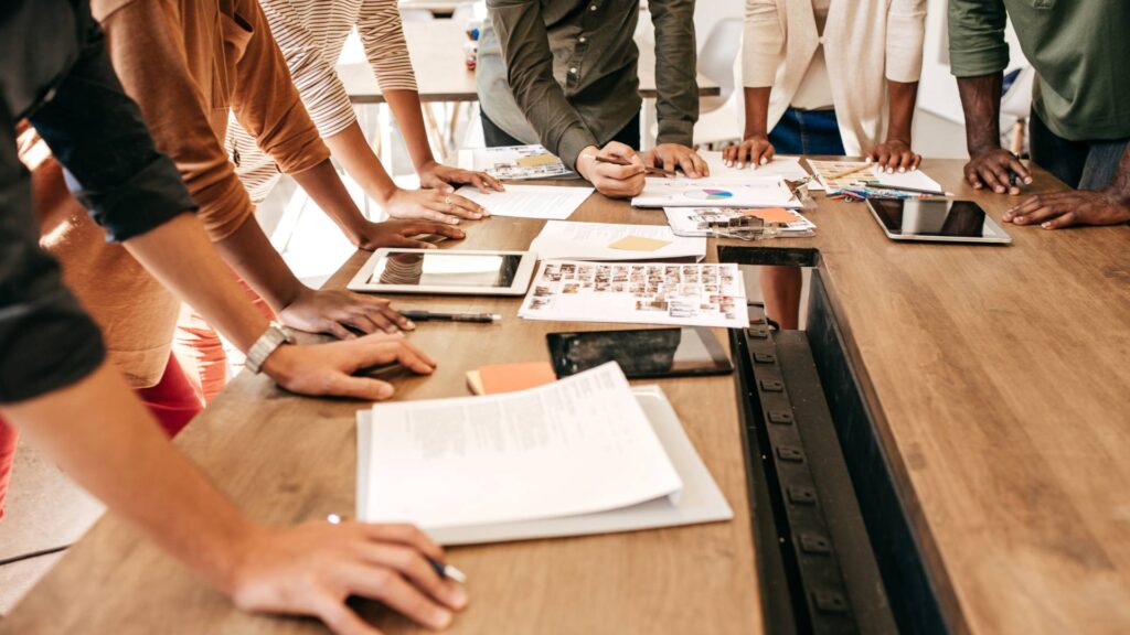 A group of people stand around a conference table, demonstrating brand consulting.