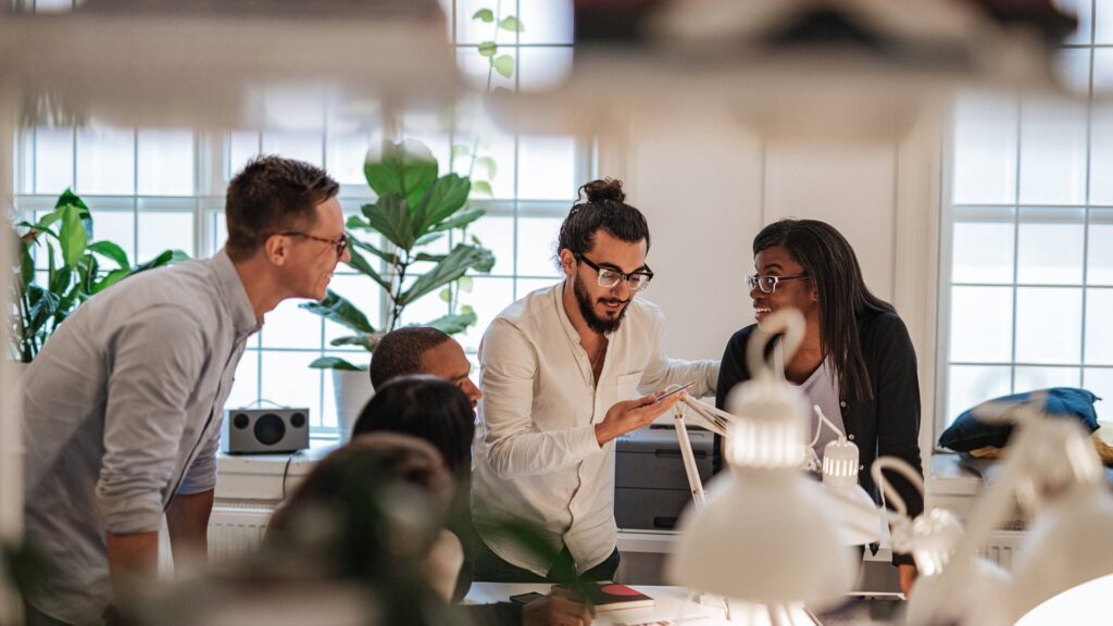 A team of people stand around a table and work together, demonstrating a start up.