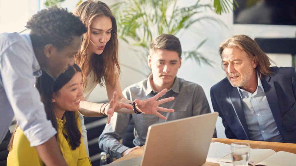 A group of people sit at a table around a laptop and receive startup consulting.