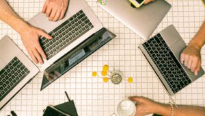 A group of silver laptops is displayed from above against a tile table. There is a glass of water and a vase of small yellow flowers displayed. This is demonstrating seo services.